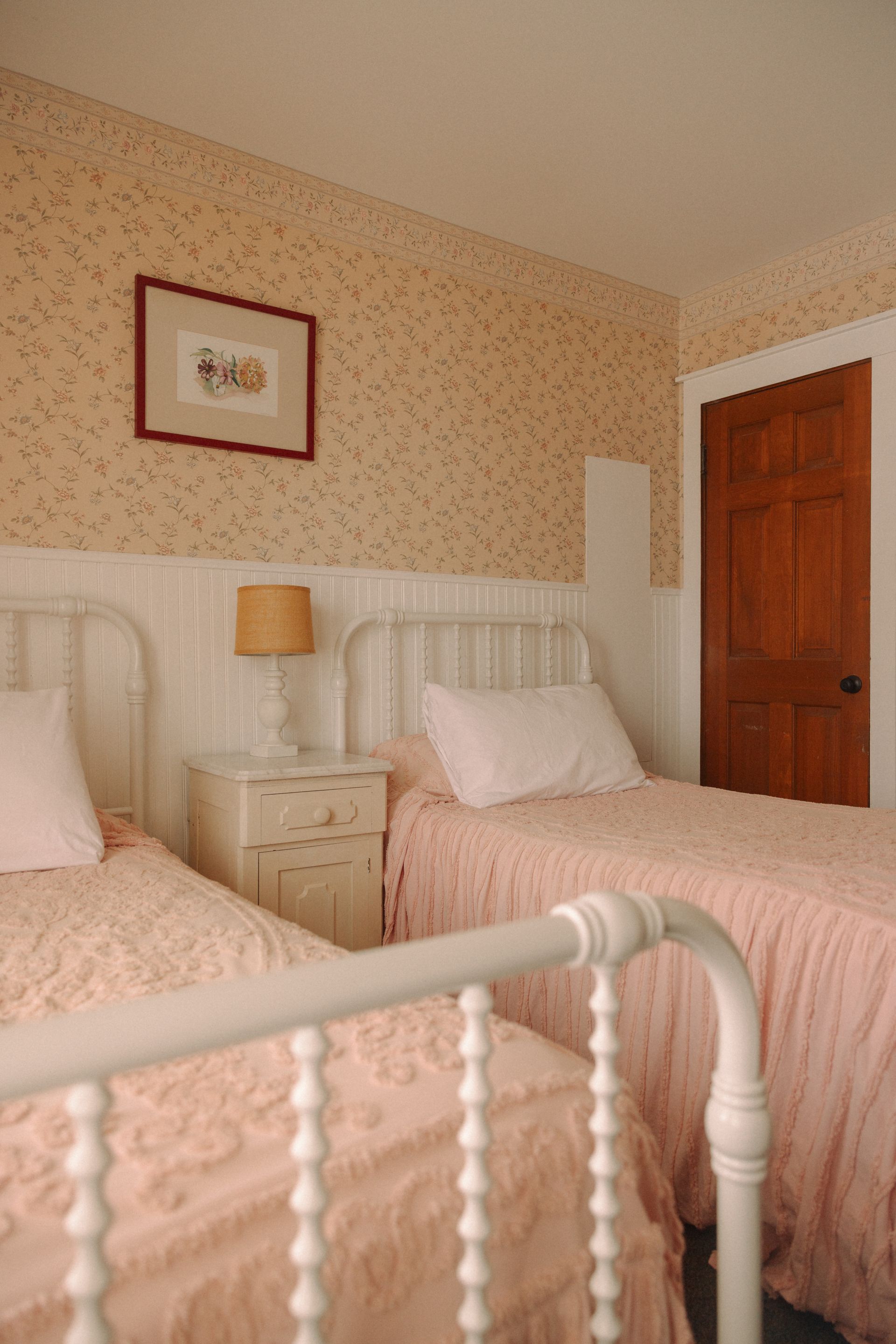 A bedroom with two beds , a nightstand and a picture on the wall.