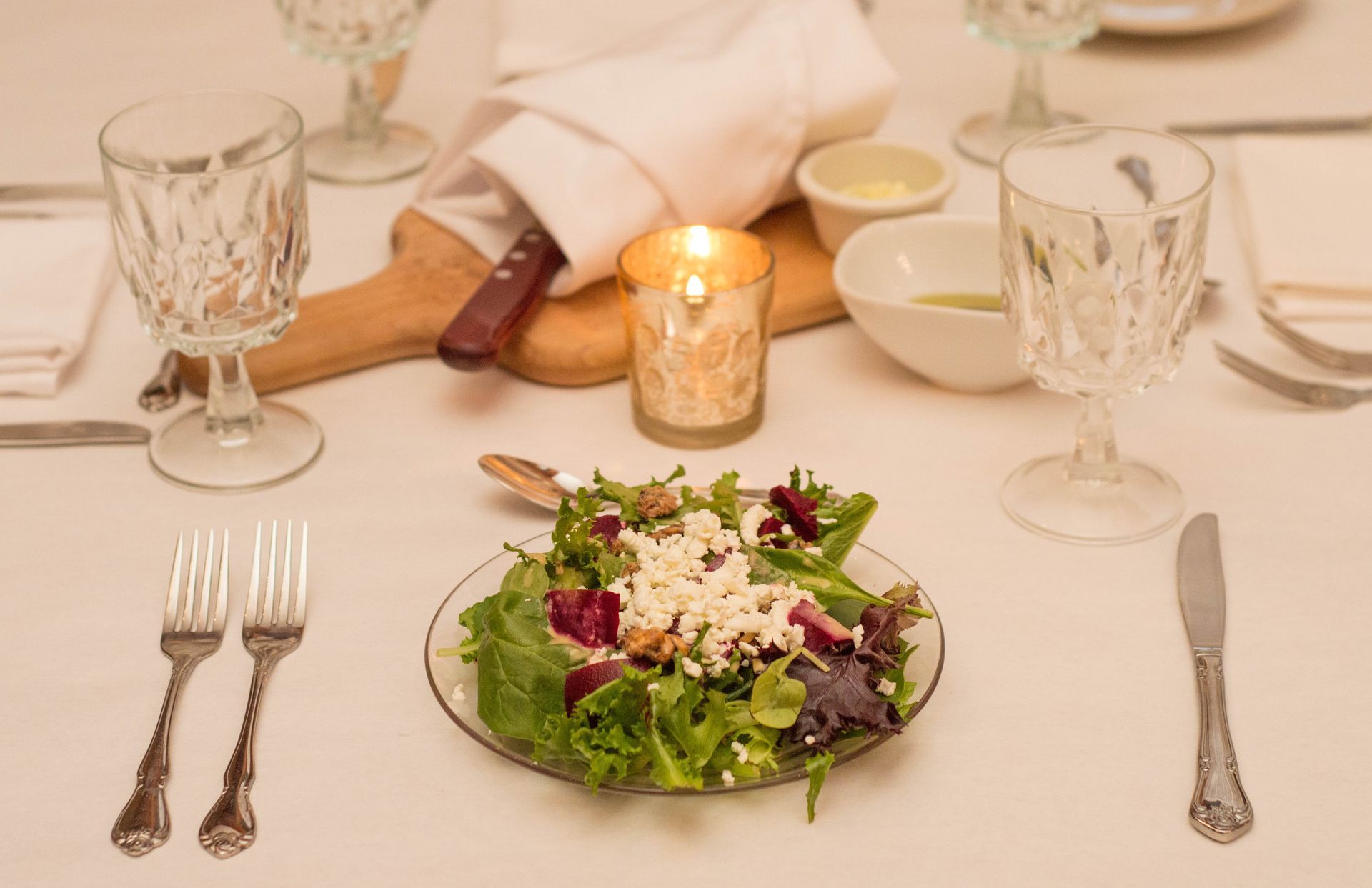 A plate of salad is sitting on a table next to a candle.