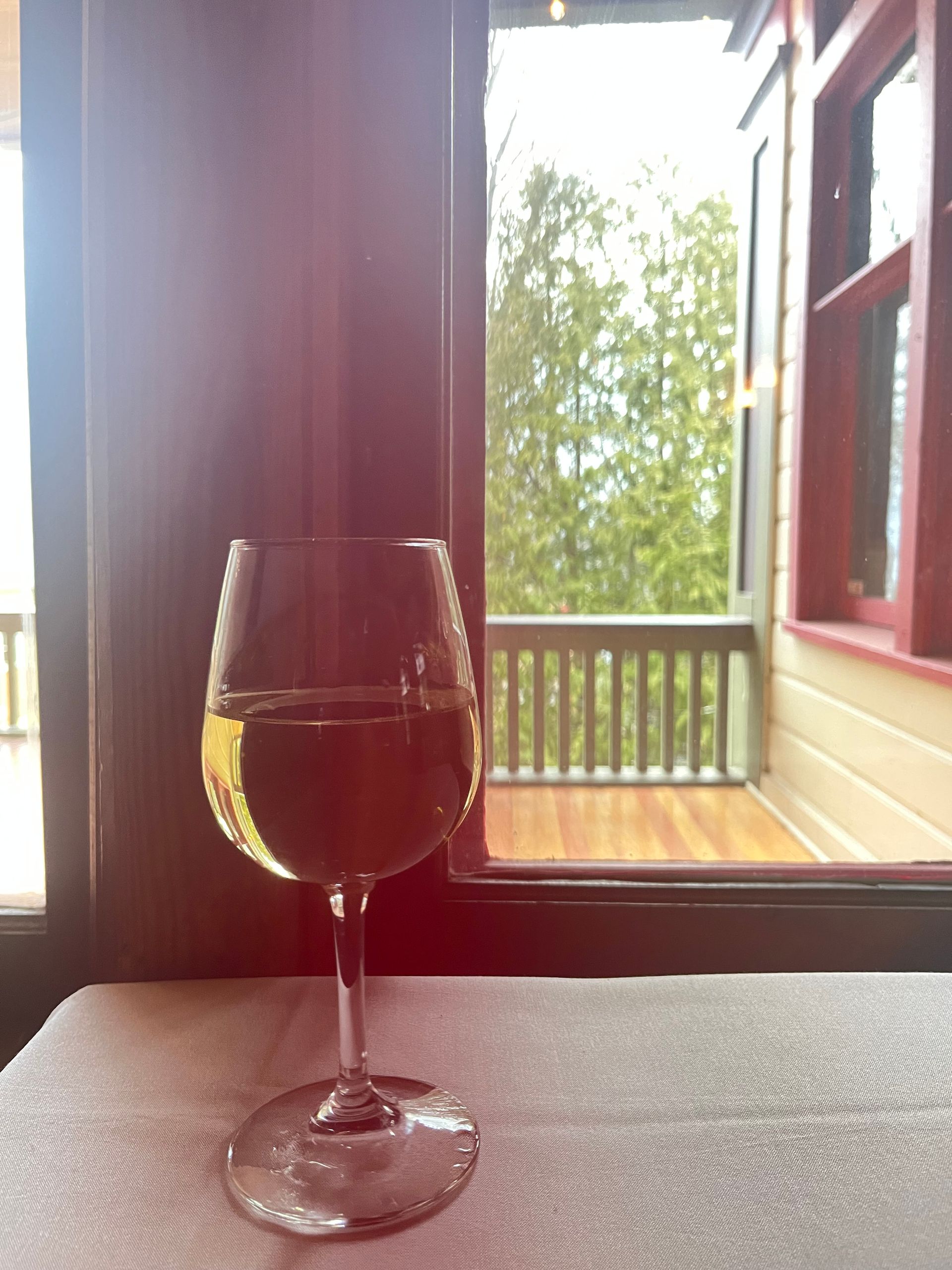 A glass of wine is sitting on a table in front of a window.
