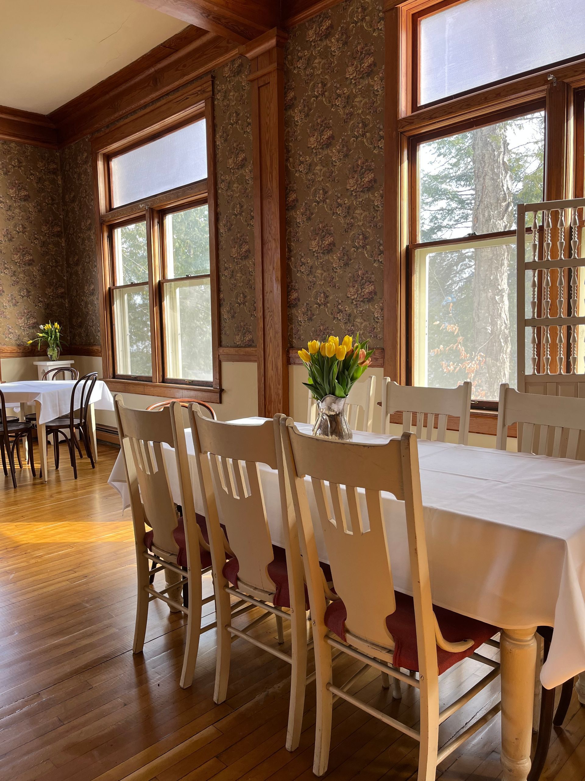 A dining room with tables and chairs and a vase of flowers on the table.