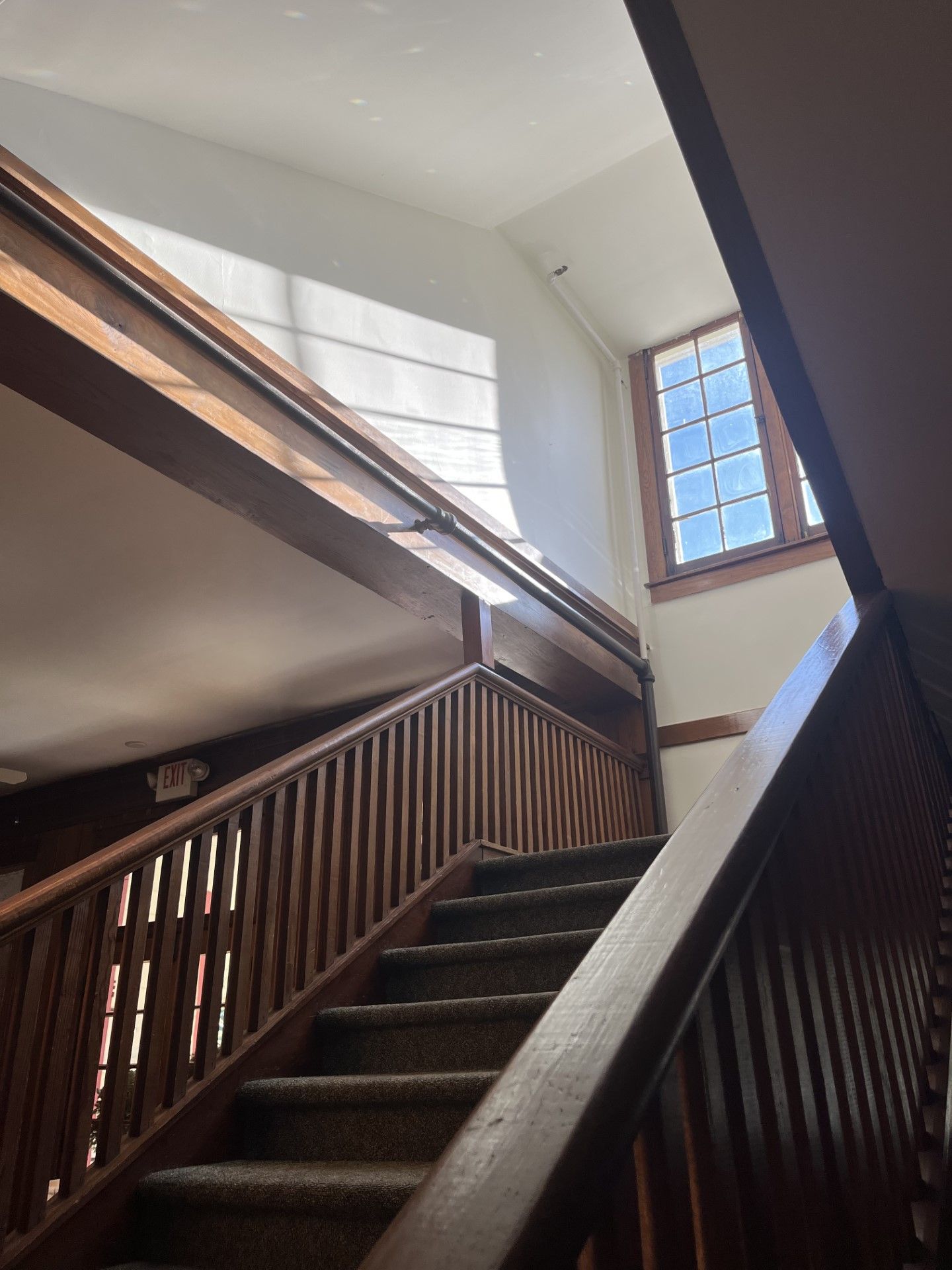 Looking up at a wooden staircase with a window in the background.