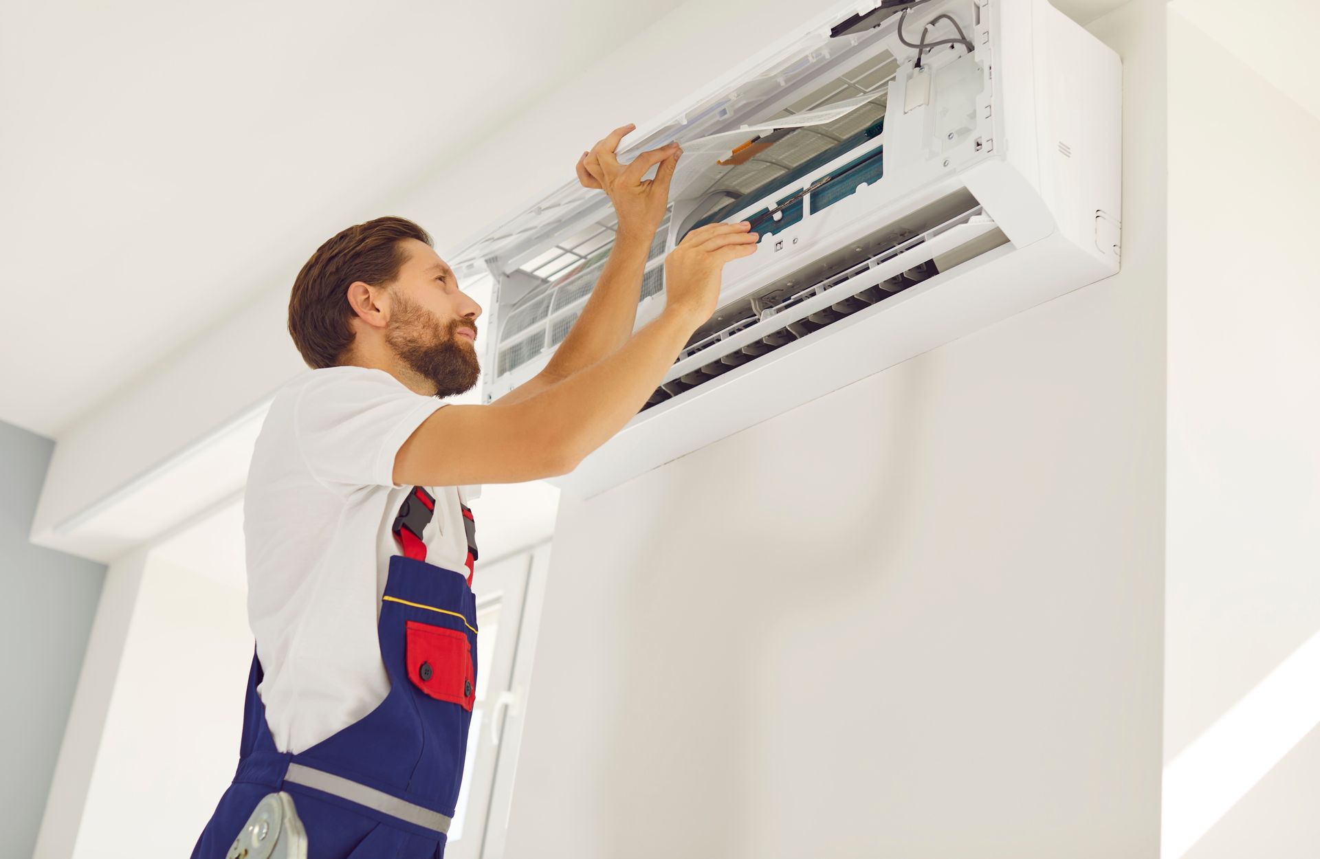 Man in overalls working on a mounted air conditioning unit.