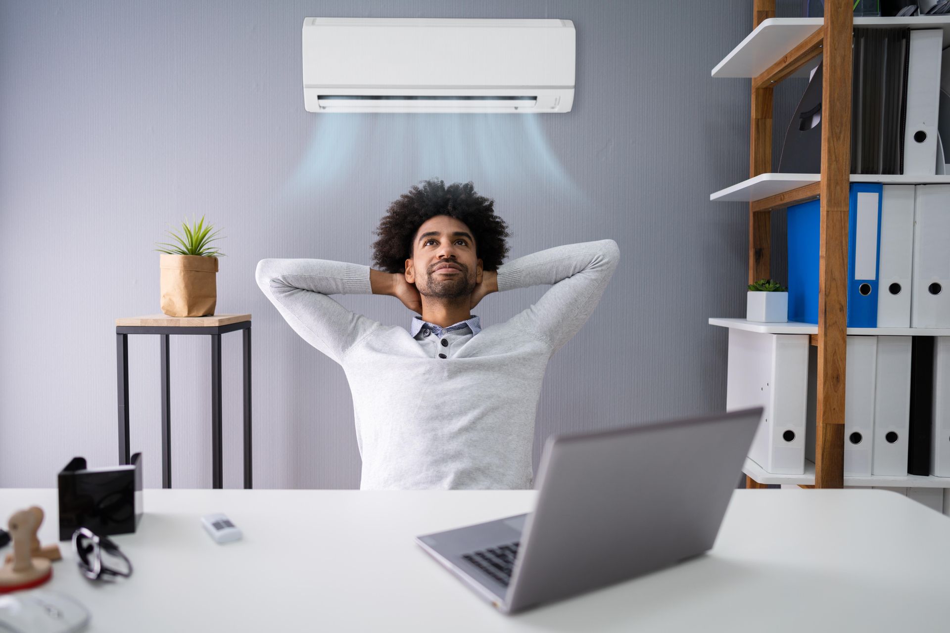 Man relaxing at a desk with laptop and air conditioner in a bright office