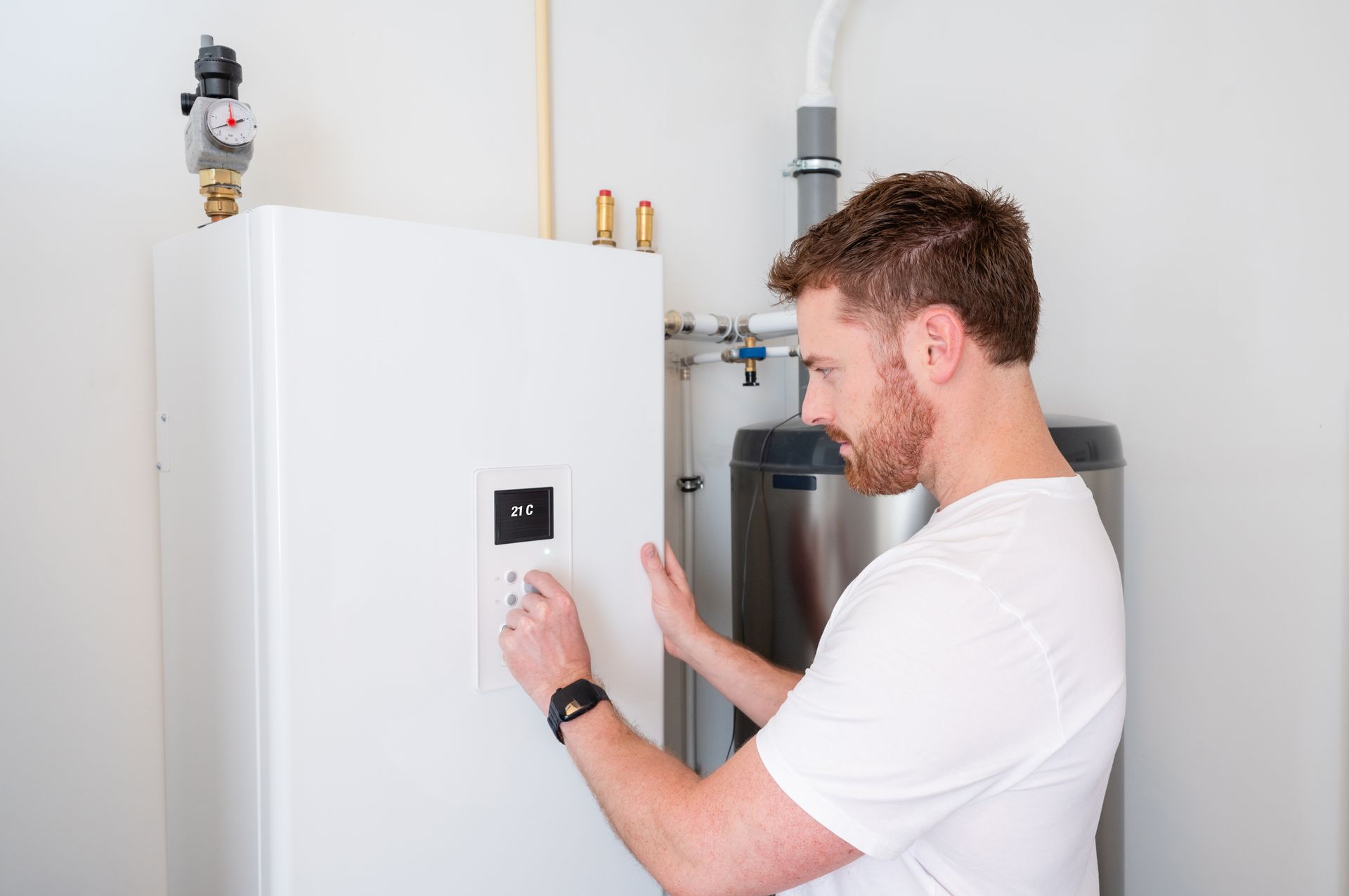 Man adjusts control panel on a white water heater in a utility room.