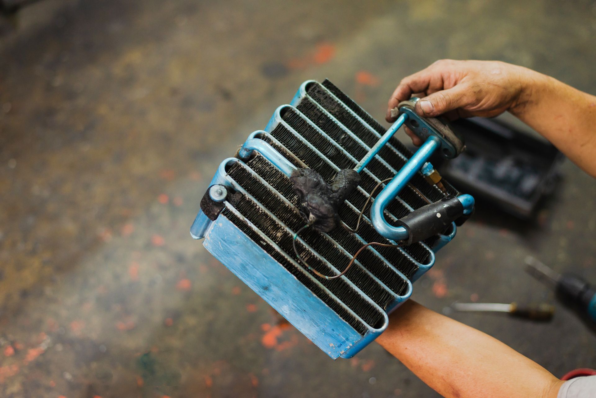 Person holding a blue and black heat exchanger, possibly for an AC unit, in a workshop.