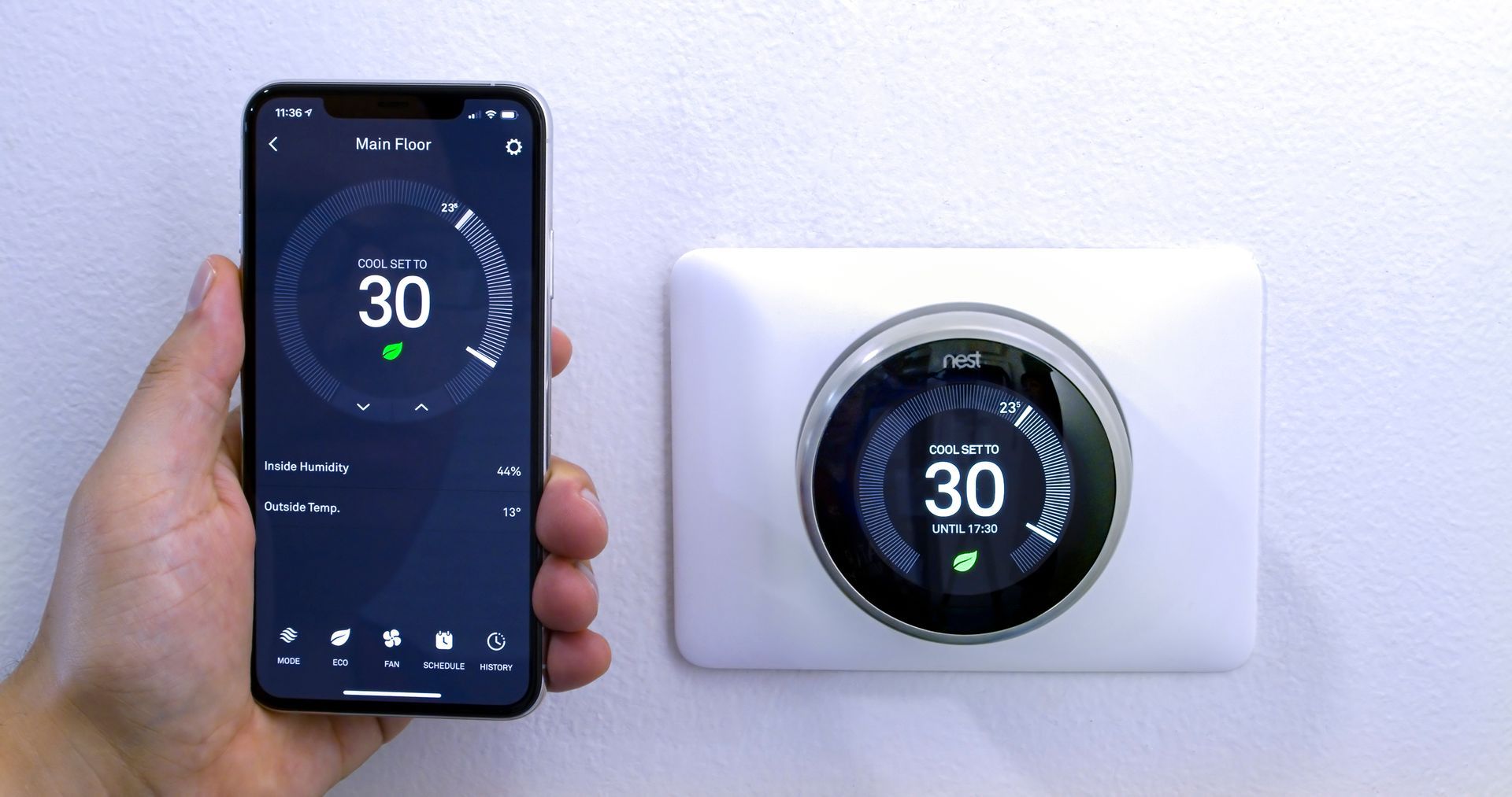 A person is holding a cell phone next to a thermostat.
