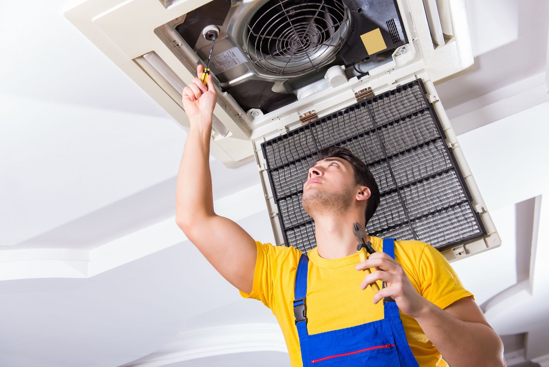 A man is fixing an air conditioner with a screwdriver.