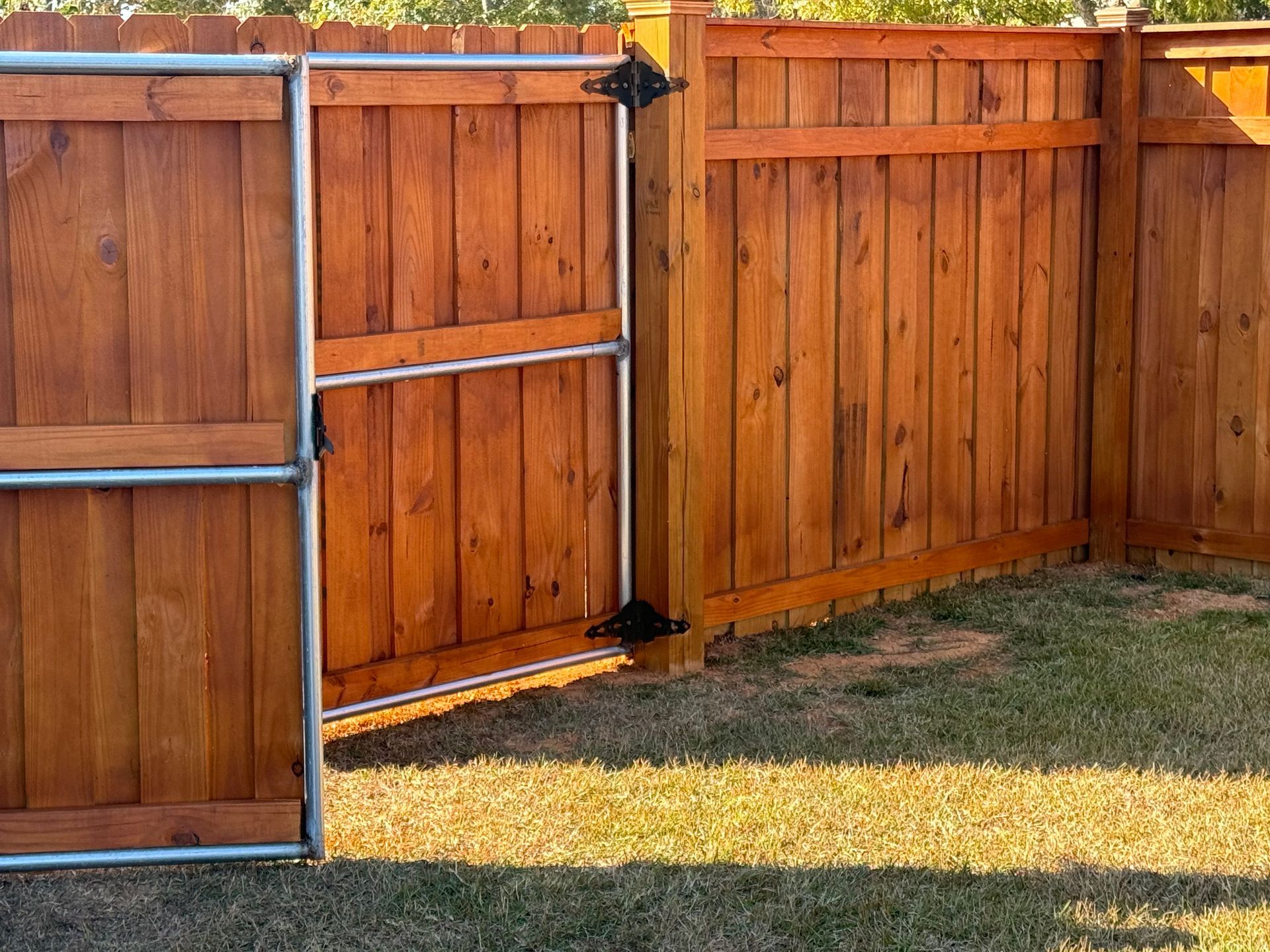 Wooden fence with a gate, stained a warm brown, in a grassy yard.