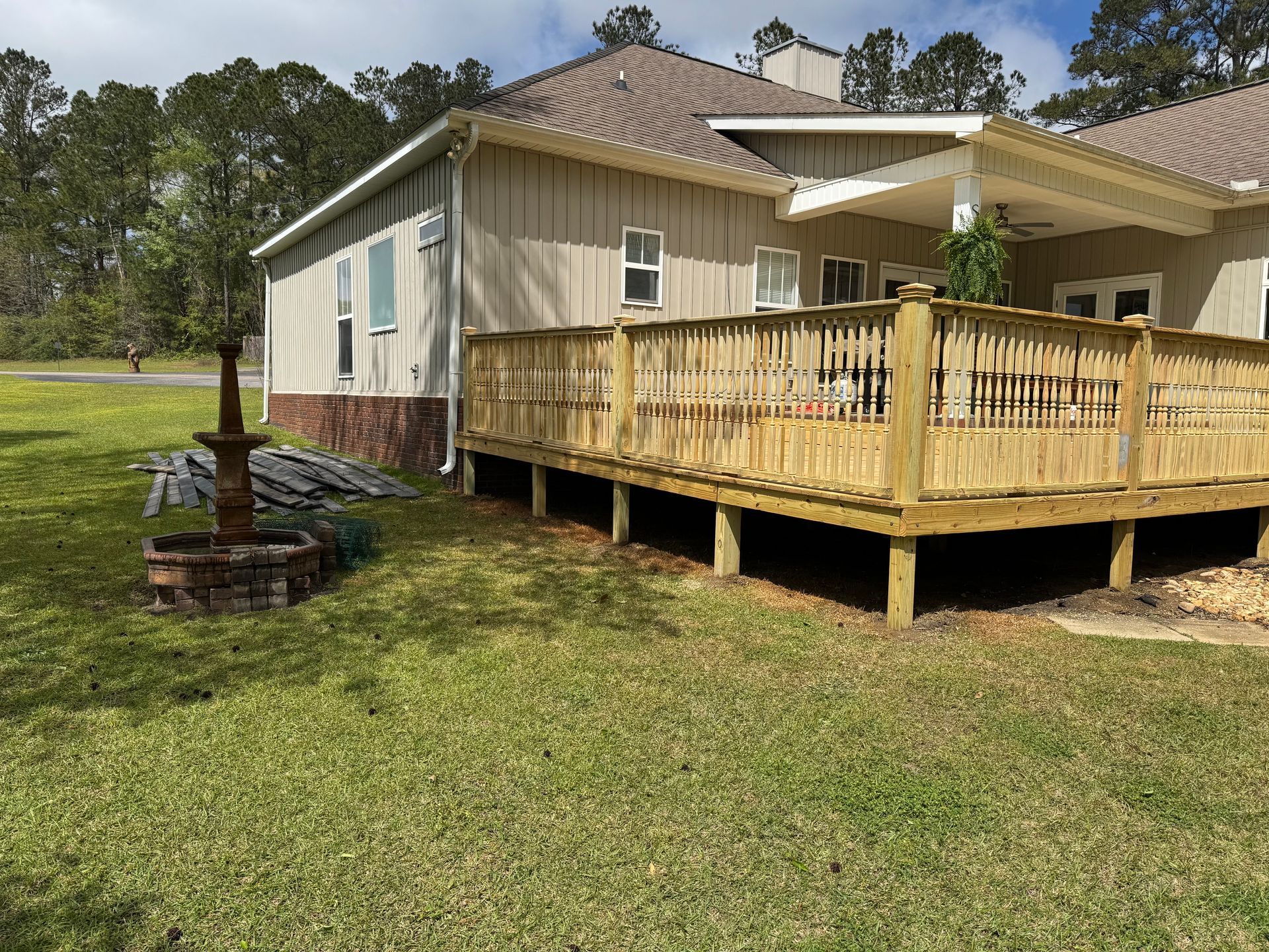 Backyard with wooden deck, fountain, and beige house on a sunny day.
