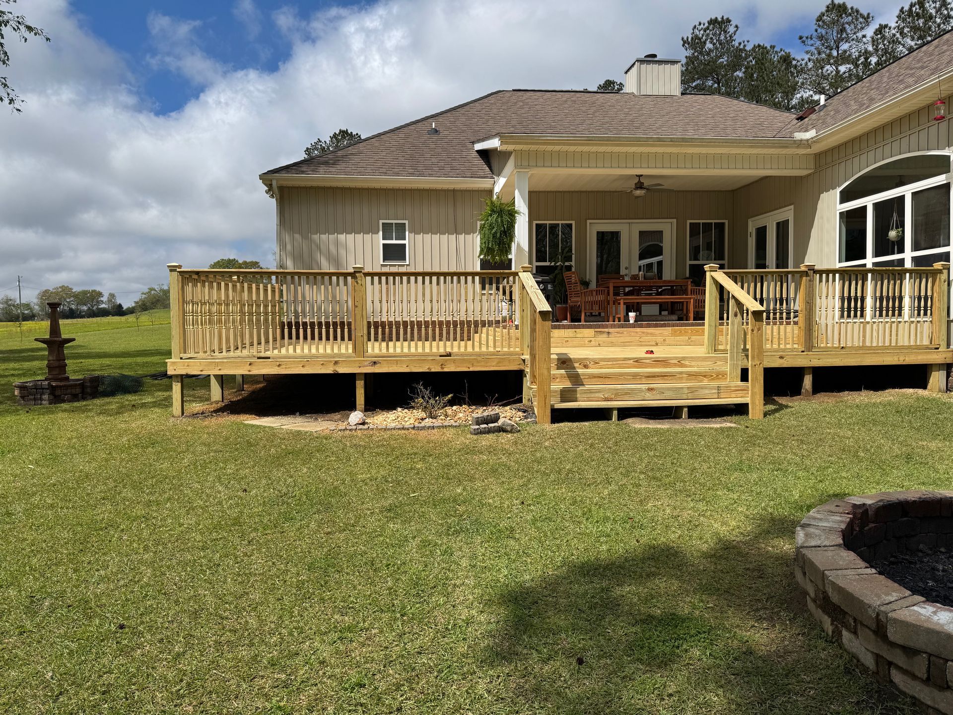 Wooden deck attached to a beige house, steps leading down to a grassy yard. Blue sky.
