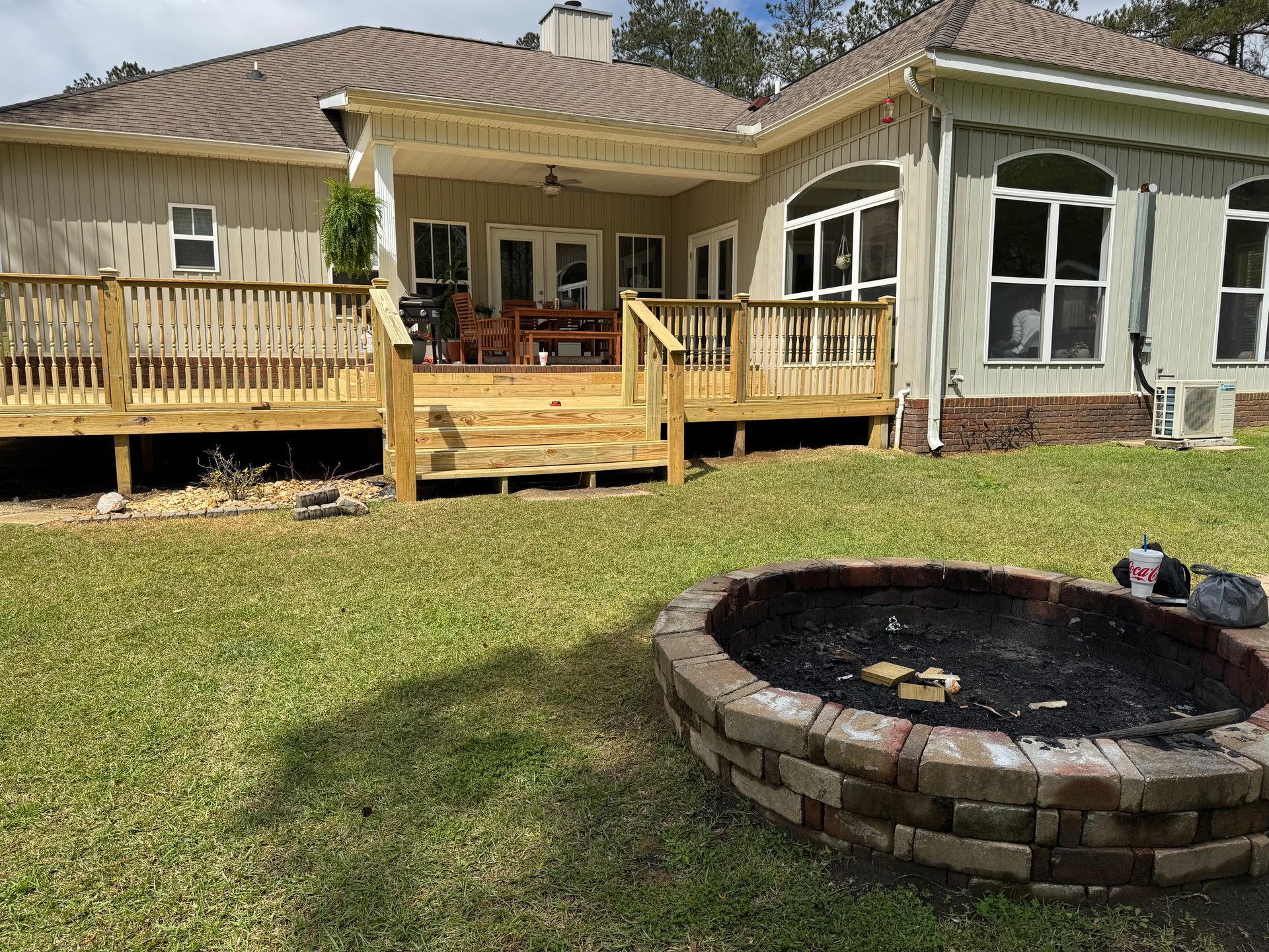 Wooden deck with a brick fire pit in a grassy backyard.