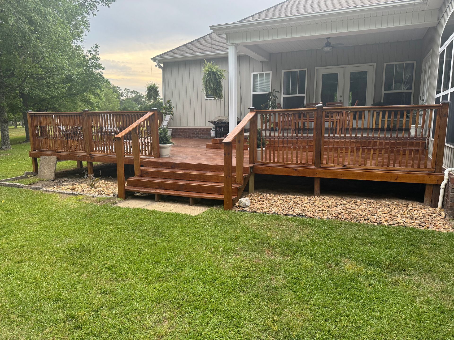 A wooden deck with steps, railings, and brown stain. It is surrounded by green grass and a building.