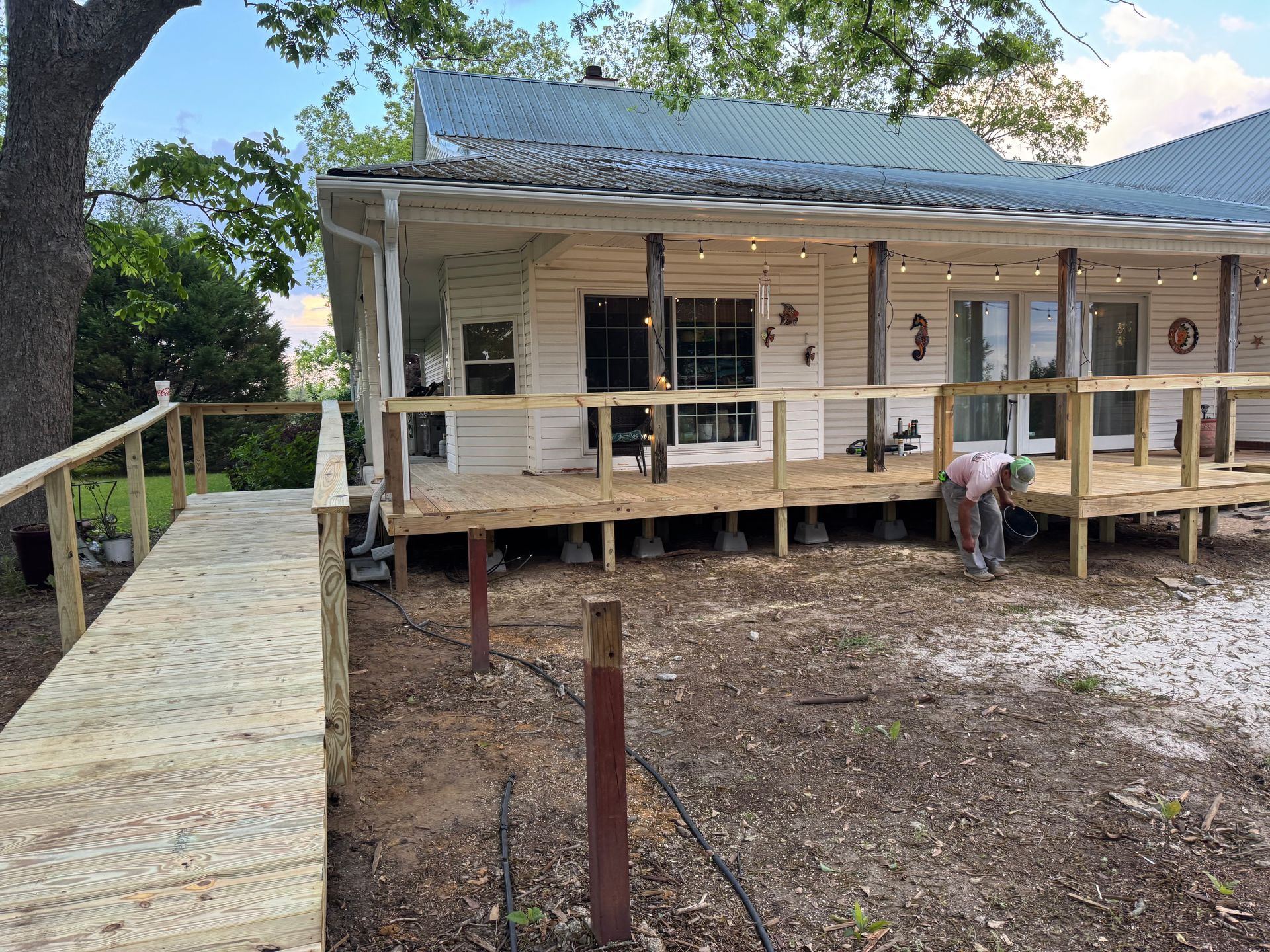 White house with a wooden deck and ramp, a person working underneath the house.