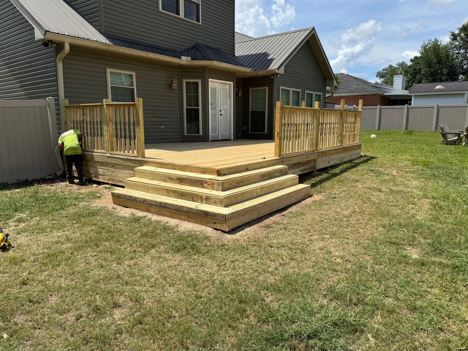 Wooden deck with steps in a backyard, partially built. A person is working on the deck.