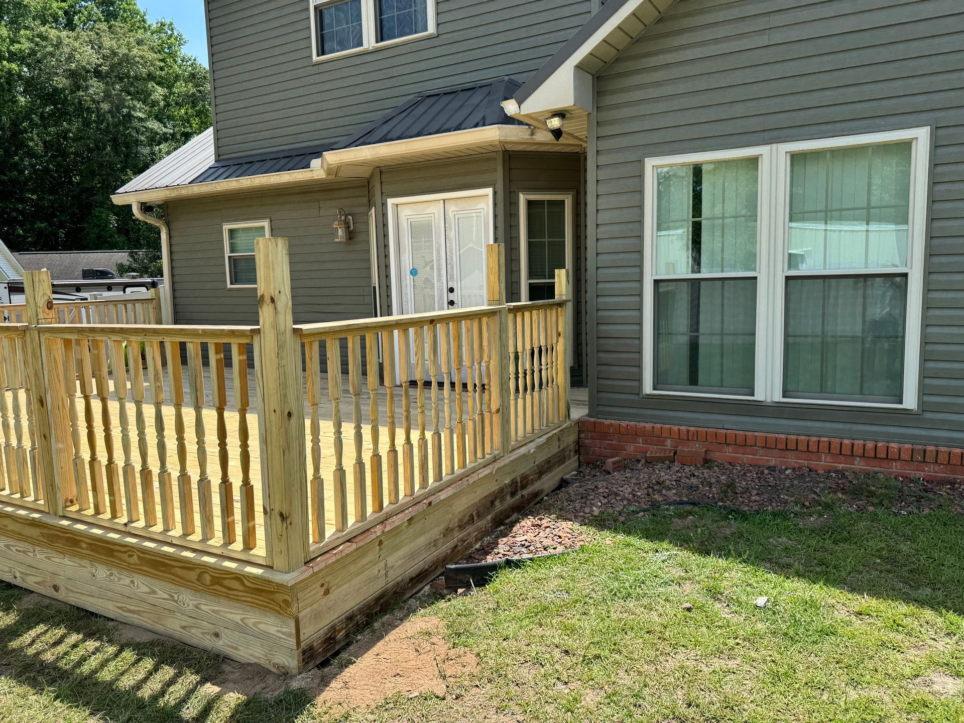 Wooden deck attached to a gray house, with grass and a small porch.