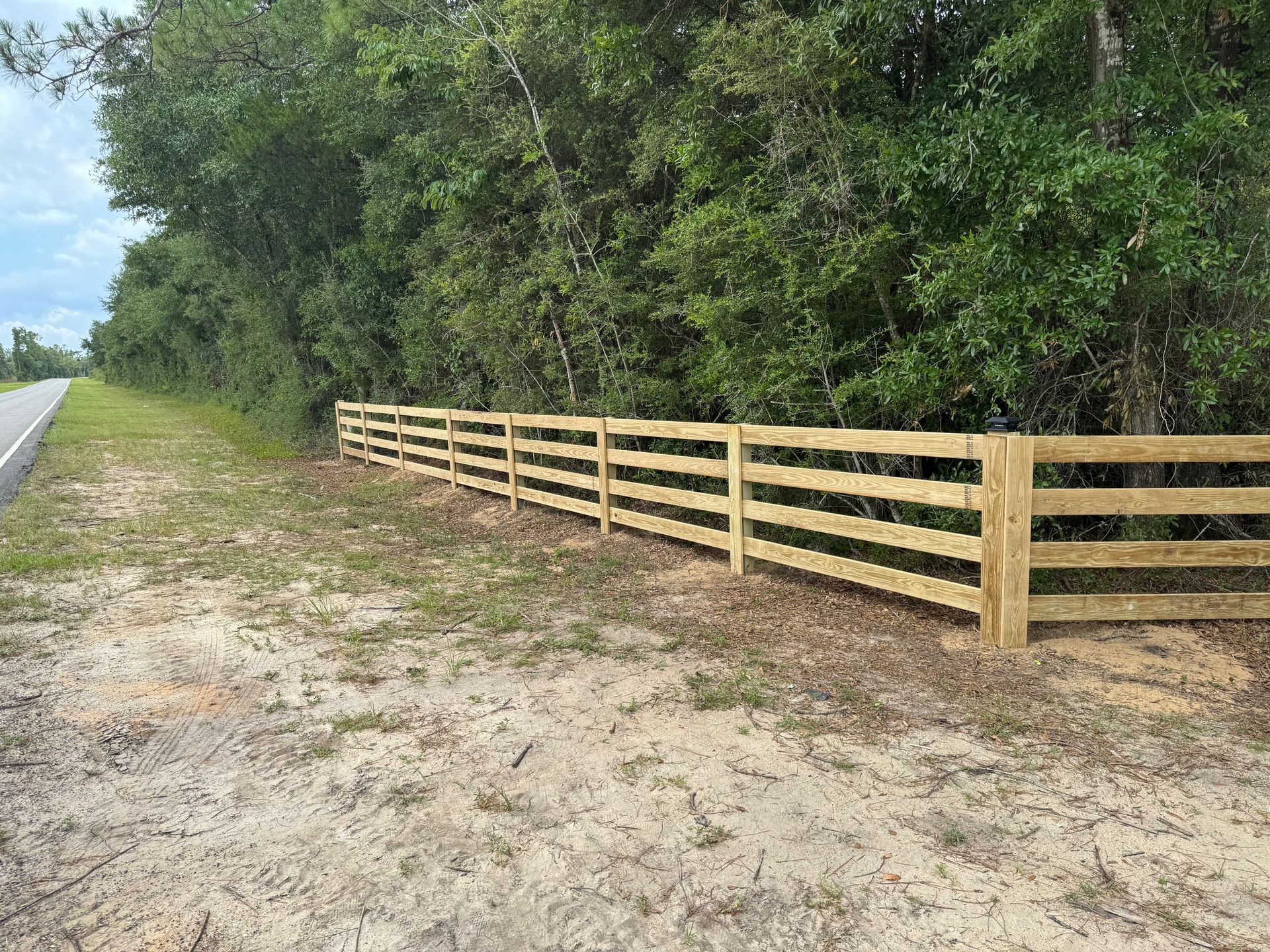 Wooden fence bordering a road next to a wooded area.