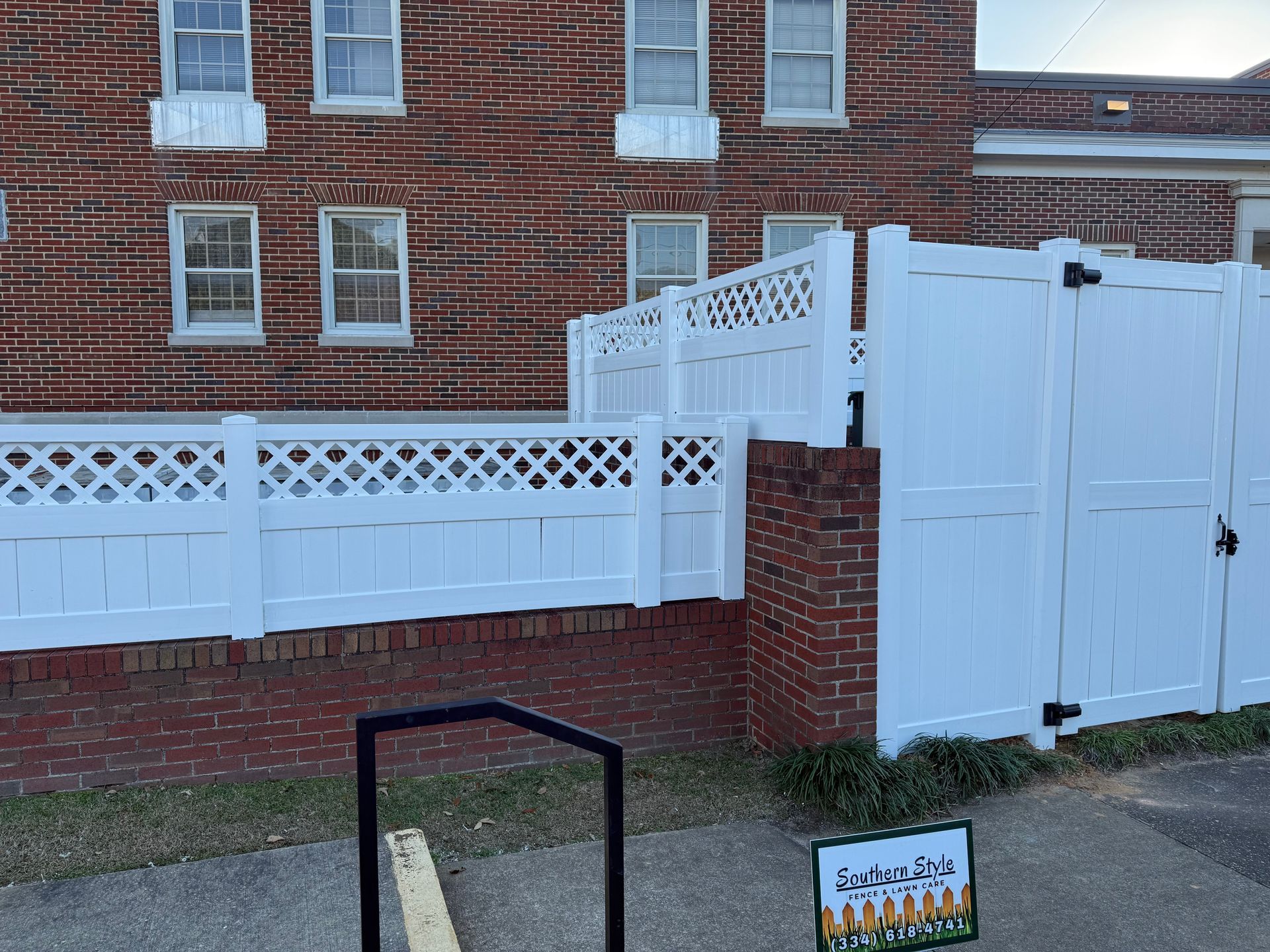 White lattice-topped fence with a gate in front of a brick building.