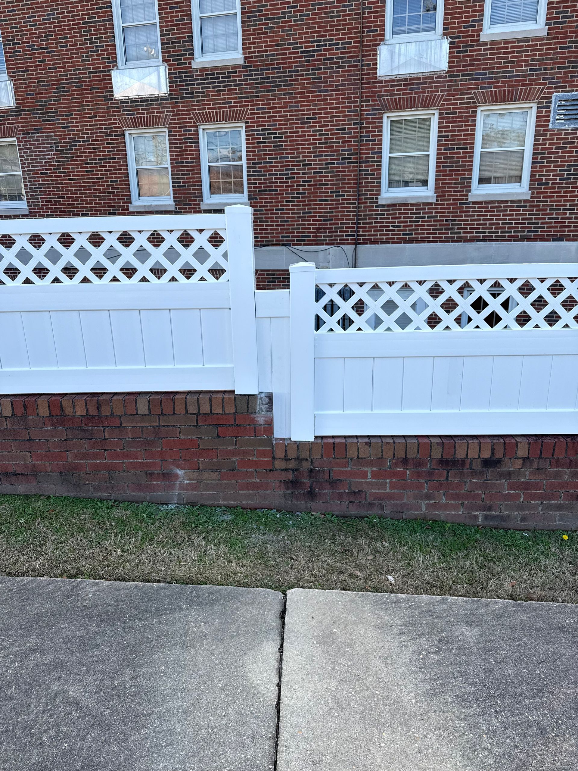White lattice fence on brick wall in front of a brick building.