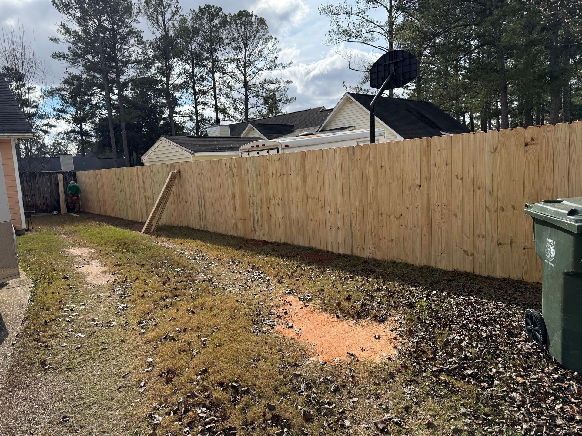 Wooden fence in a backyard with a basketball hoop visible.