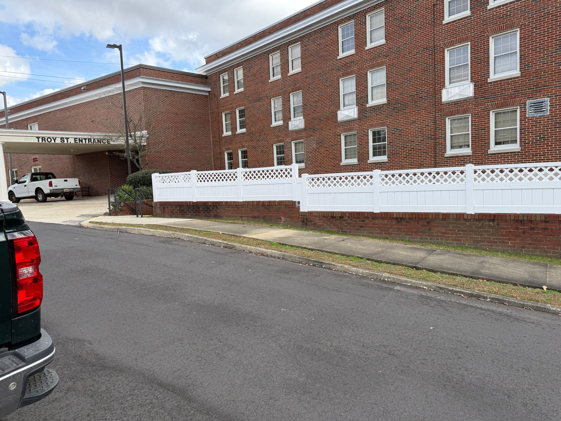 Brick building with white fence, truck entering a covered entrance.