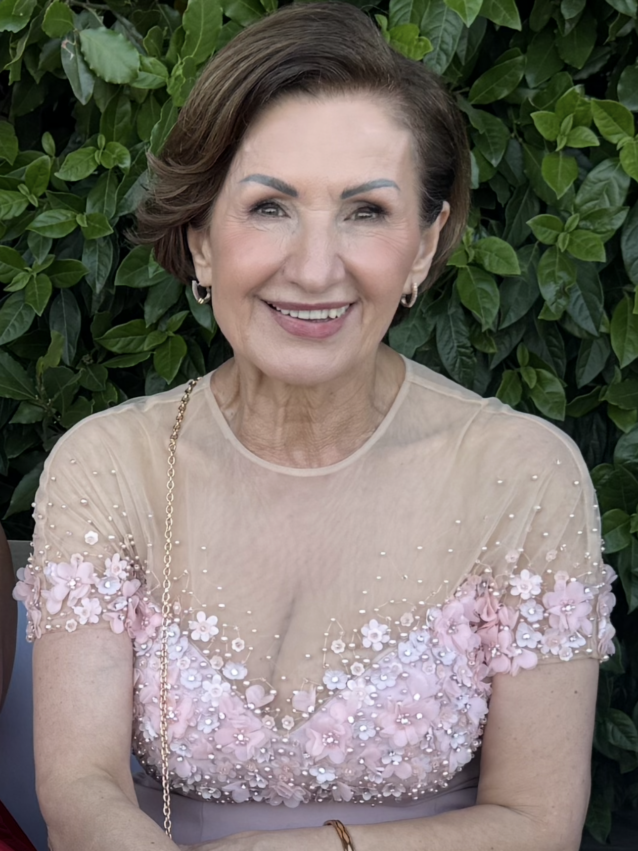 A woman in a blue shirt and pearl necklace is smiling for the camera.