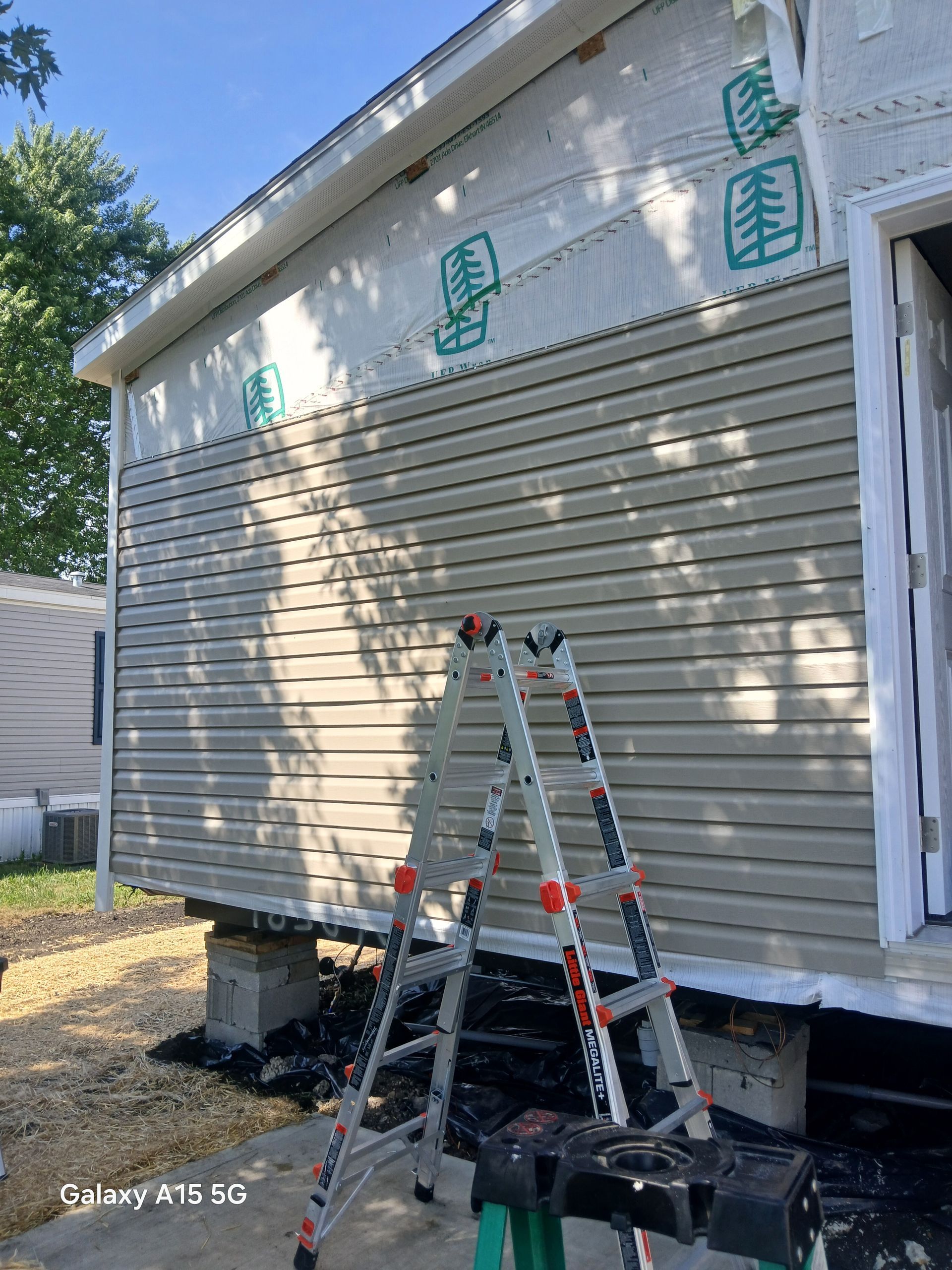 House exterior with installed tan siding. A ladder is in front of the siding.