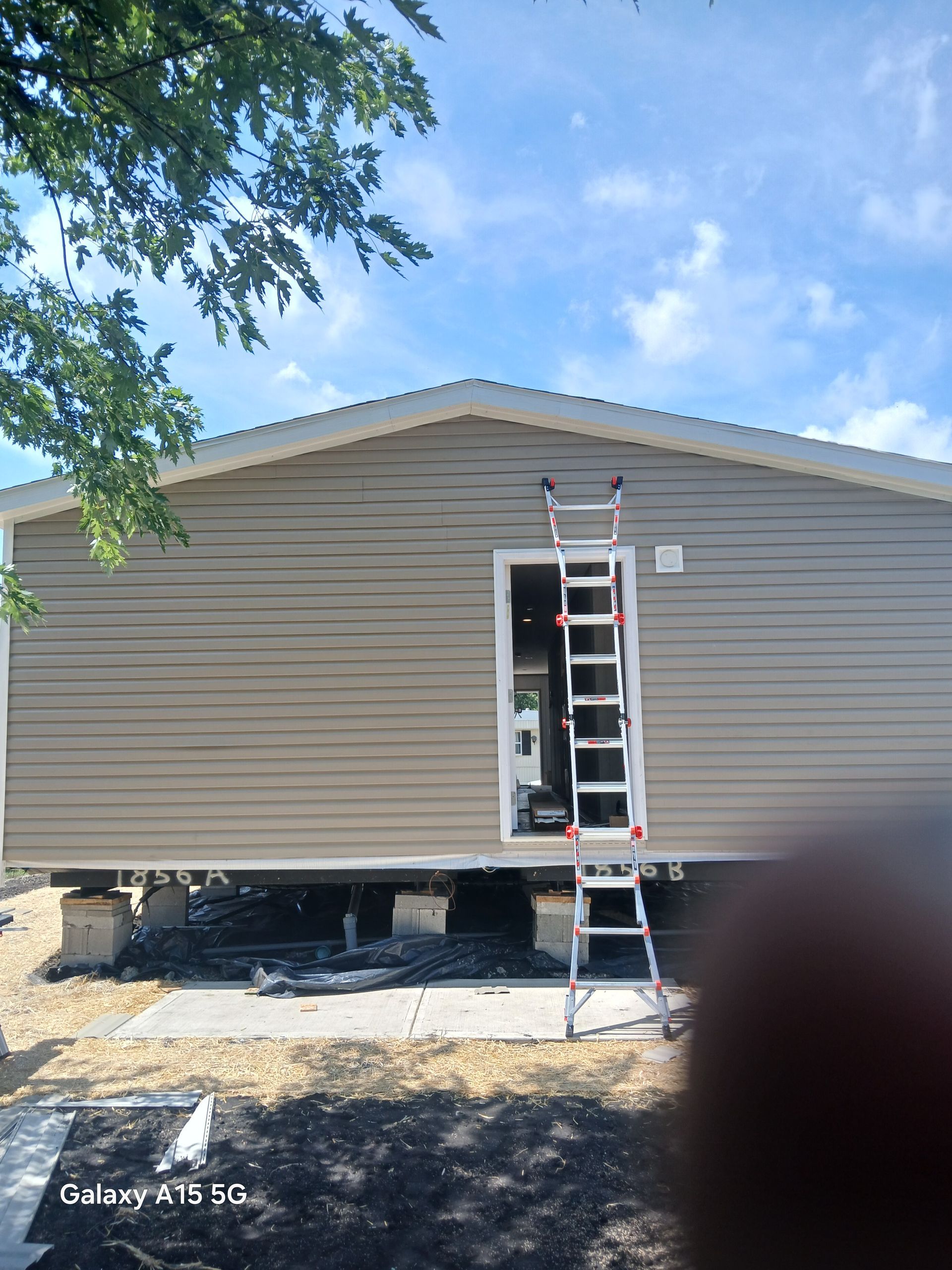 Tan-sided building with open doorway. A ladder rests against the doorway. Blue sky with clouds.