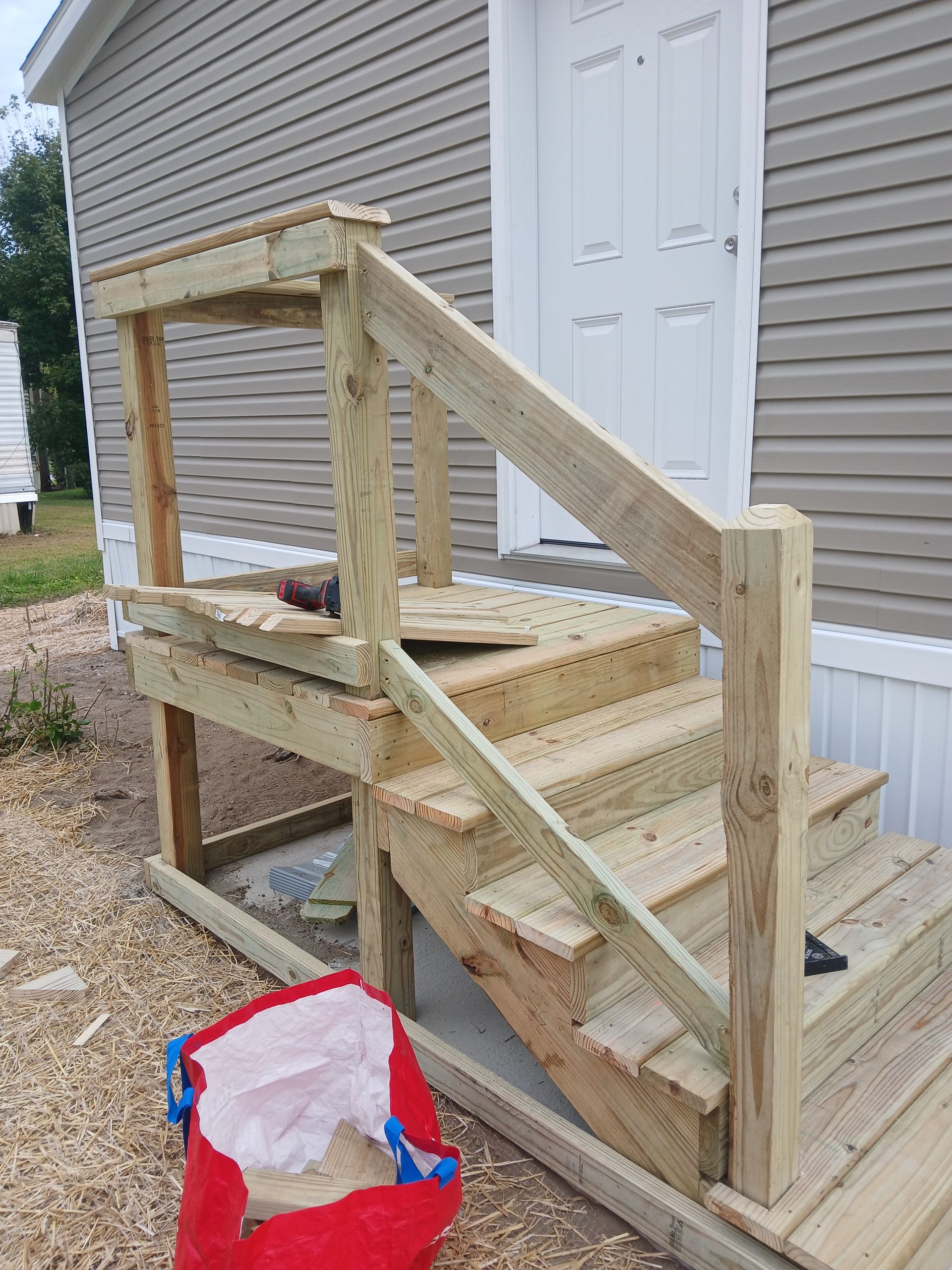 Wooden outdoor staircase and landing leading to a white door; construction materials visible.