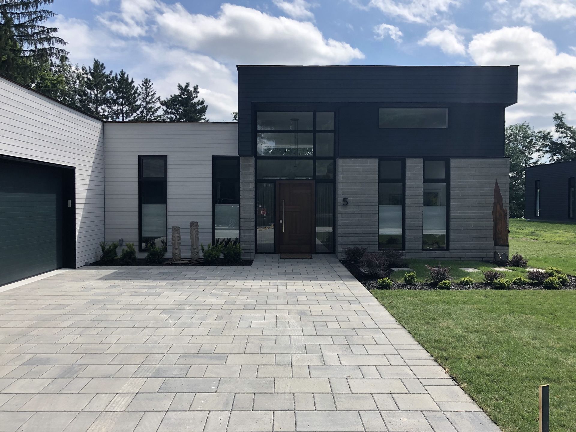 Une maison moderne de plain-pied avec un bardage horizontal blanc et gris, des boiseries foncées, une porte d'entrée en bois et une allée pavée.