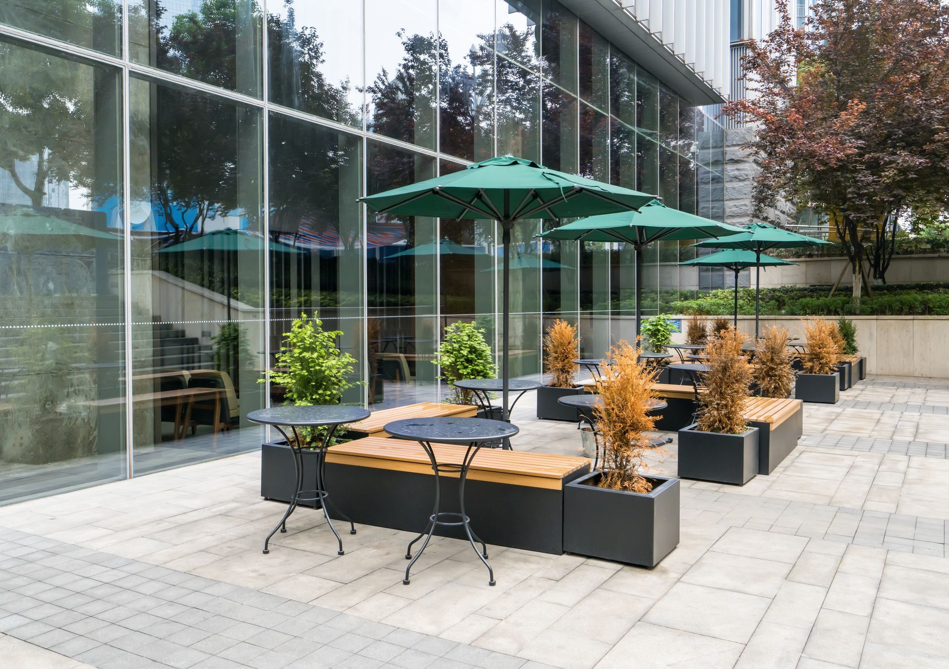 Terrasse extérieure avec parasols verts, tables et bancs devant un bâtiment moderne.
