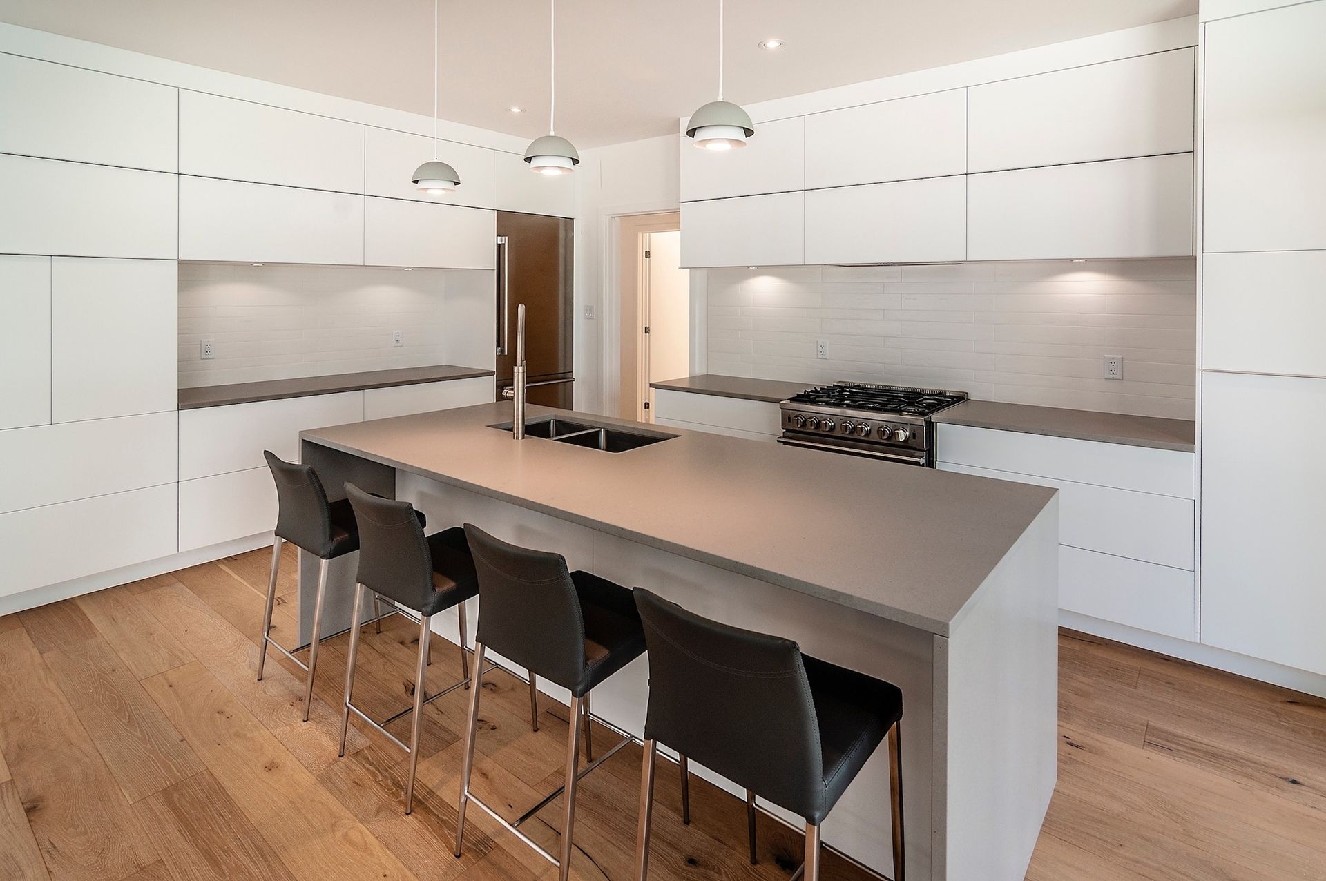 Cuisine moderne avec îlot gris, armoires blanches, électroménagers en acier inoxydable et plancher en bois.