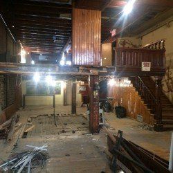 Intérieur d'un bâtiment en rénovation; poutres en bois, escalier et planchers apparents.