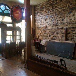 Intérieur d'un bar avec des murs en pierre et une porte ouverte, un panneau Budweiser et des débris de construction.