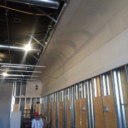 Chantier : charpente métallique, cloisons sèches, plafond incurvé. L'ouvrier se tient près du mur.