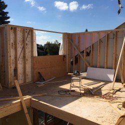 Chantier de construction. Charpente en bois des murs d'un bâtiment sous un ciel bleu. Scie et matériaux présents.