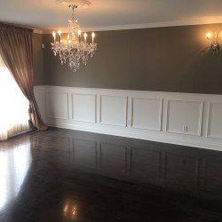 Pièce vide avec parquet en bois foncé, lambris blancs et mur marron. Lustre en cristal.