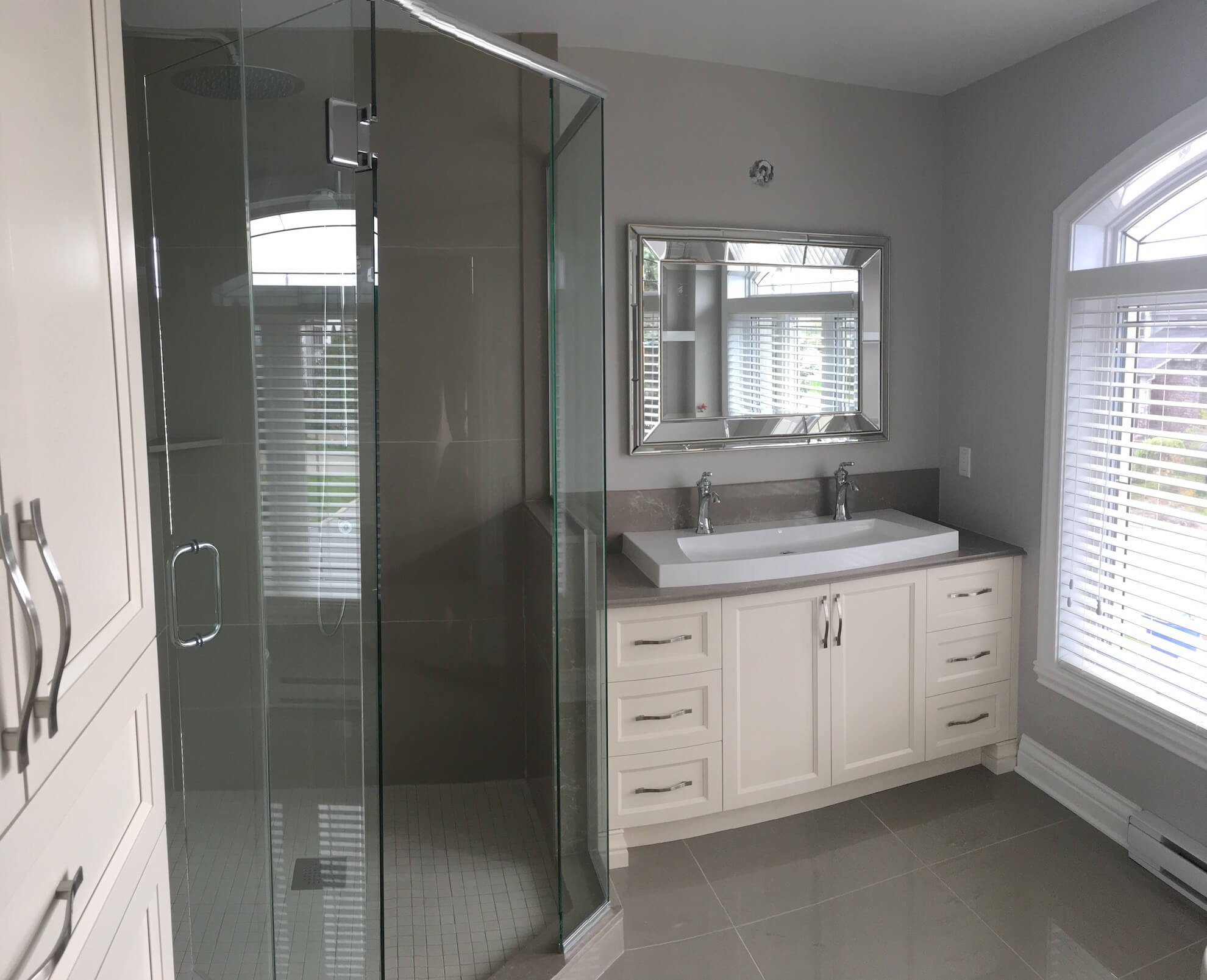 Salle de bains moderne avec douche d'angle en verre, meuble-lavabo double blanc avec lavabo rectangulaire, miroir et stores blancs.