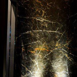 Mur en marbre noir avec veines dorées et blanches, reflétant la lumière.