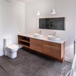 Salle de bain moderne : meuble vasque en bois avec double vasque, WC, sol en carrelage gris et deux suspensions.