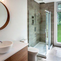 Salle de bain moderne avec douche, toilettes, lavabo et grande fenêtre avec vue extérieure verdoyante.