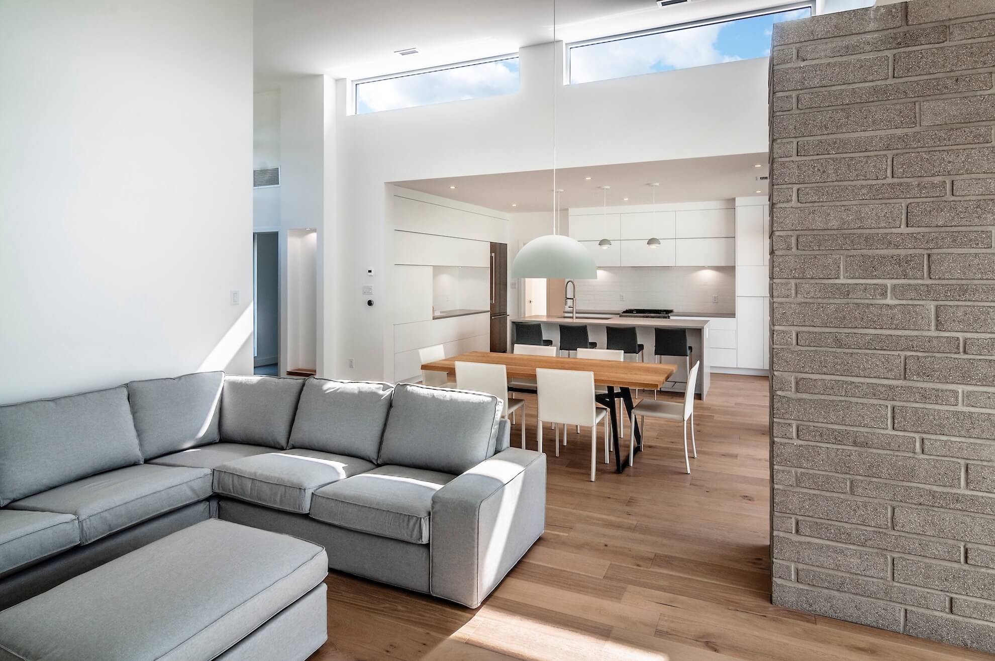 Salon moderne avec un canapé sectionnel gris, parquet, coin repas et cuisine blanche.