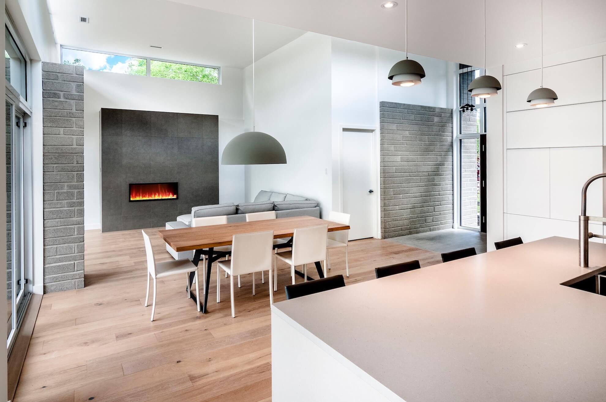 Espace de vie moderne à aire ouverte avec coin repas, cheminée et cuisine avec murs blancs et planchers de bois clair.