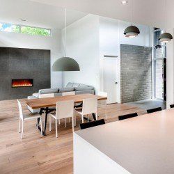 Intérieur moderne et minimaliste avec table à manger, coin salon et cheminée. Parquet clair, touches de gris et suspensions.