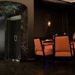Intérieur de restaurant avec des chaises orange, des murs noirs et une porte encadrée de marbre.