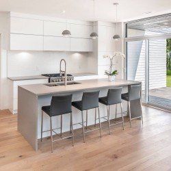 Cuisine blanche moderne avec îlot central gris, banquettes et plafonniers. Porte coulissante donnant sur l'extérieur.