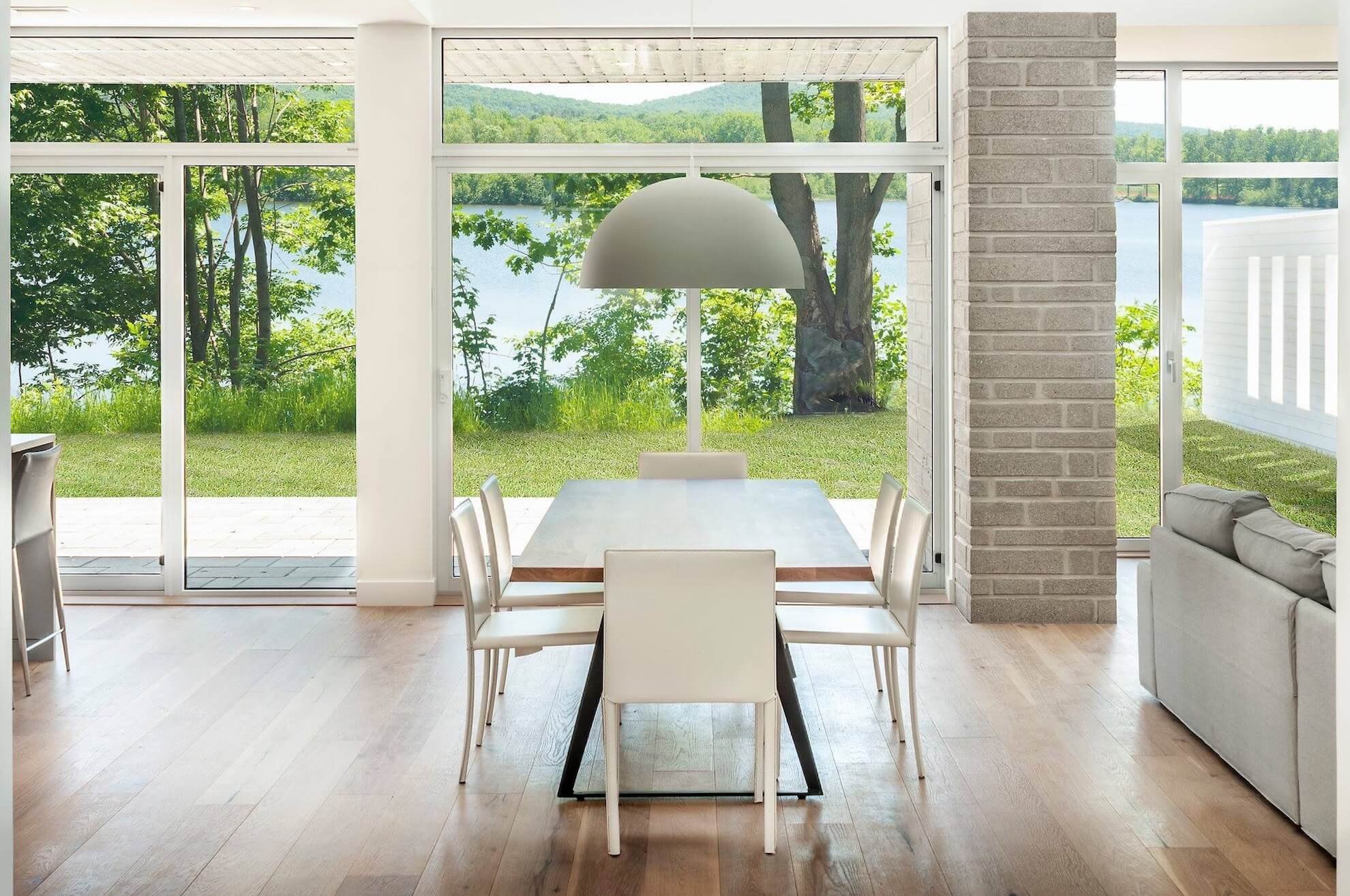 Salle à manger avec une table en bois, des chaises blanches et de grandes fenêtres donnant sur un lac.