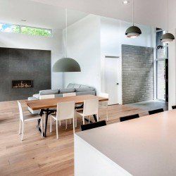 Salon moderne : parquet en bois clair, table à manger, canapé, cheminée, grandes suspensions grises et murs blancs.