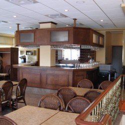 Intérieur de restaurant avec un bar en bois, des tables, des chaises et un escalier avec une rampe.