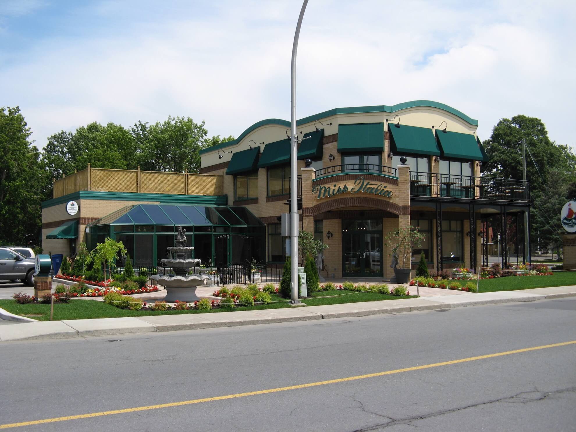 Restaurant avec auvents verts, façade en briques beiges et terrasse avec fontaine.