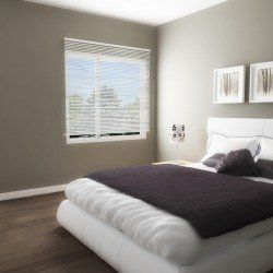 Chambre avec un lit blanc, une couverture violet foncé et une fenêtre avec stores ; les murs sont de couleur neutre.